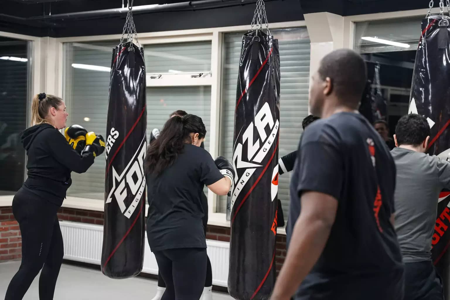 Mensen beoefenen boksen in sportschool Fightmasters en slaan op hangende bokszakken. Verschillende individuen zijn gefocust op hun training.