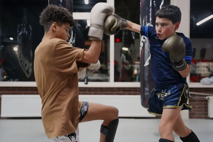 Twee leerlingen trainen samen tijdens een kickboksles. Één leerling gooit met vastberadenheid een rechtse directe op de hand van de andere leerling.