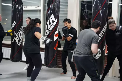 Twee jongens trainen samen in een kickboksschool. Één leerling gooit met vastberadenheid een rechtse directe op de hand van de andere leerling.