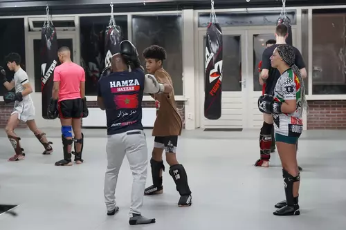 Kinderen beoefenen kickboksen in sportschool Fightmasters; sommigen werken samen aan techniek, en anderen luisteren naar uitleg van een trainer.