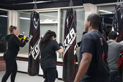 Een groep mensen doet mee aan een boksles en slaat met zware tassen in de goed verlichte en overdekte sportschool Fightmasters.