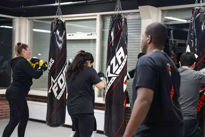 Een groep mensen die bokstechnieken beoefenen met bokszakken op de sportschool van Fightmasters.