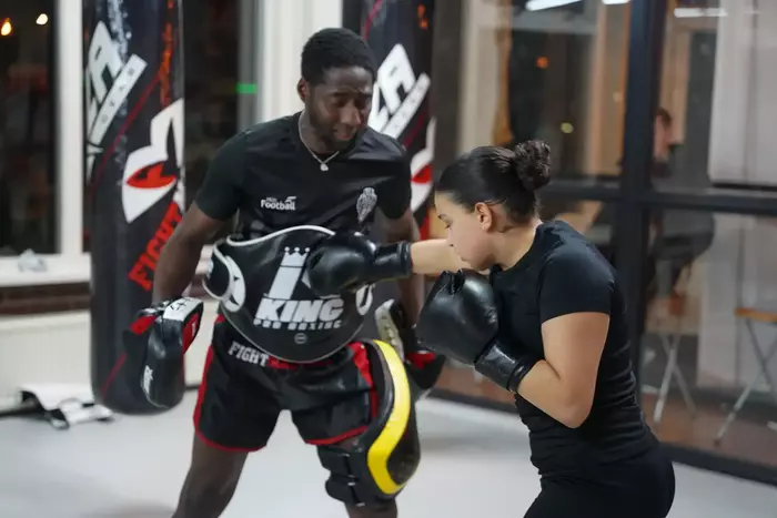 Twee jongens die aan het boksen zijn, de een in een bruin shirt en de ander in een blauw shirt, zijn bezig met een technieksessie in sportschool Fightmasters.